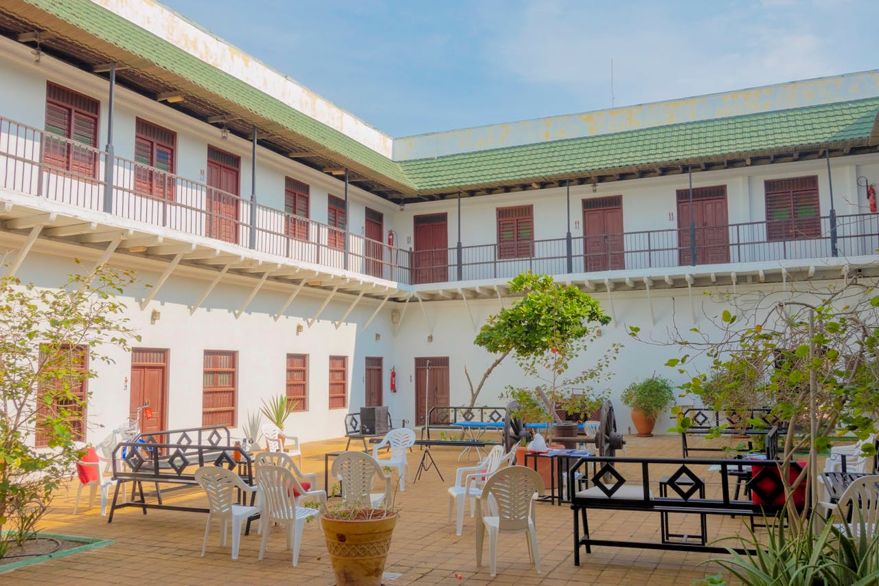 Bright courtyard with seating, surrounded by green-roofed architecture and lush plants.